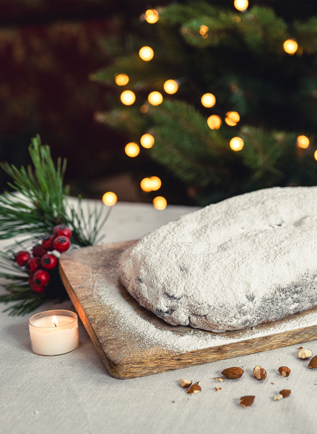 Gepuderter Mandelstollen, unangeschnitten auf Schneidebrett neben einem Teelicht, weihnachtlich