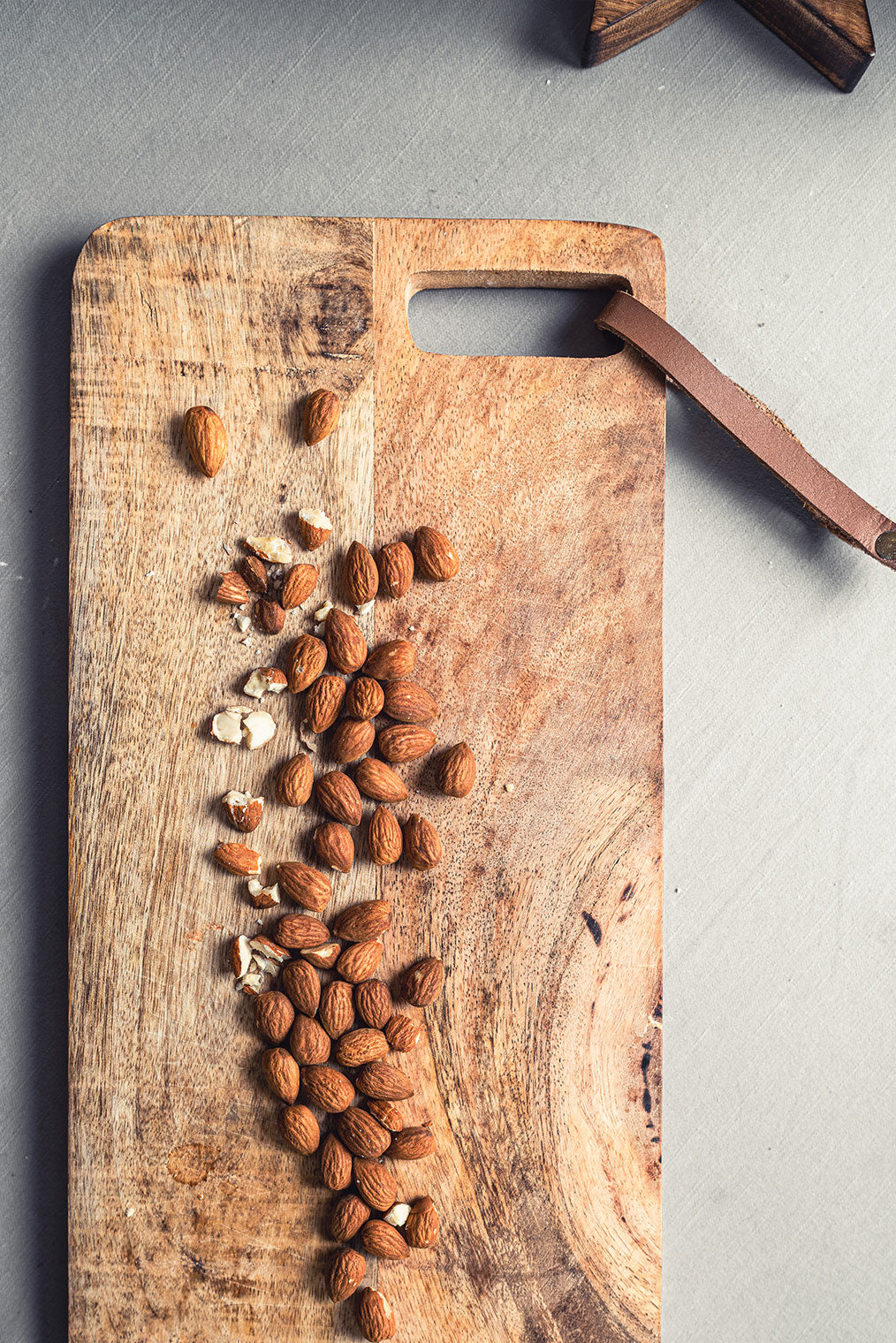 Schneidebrett mit Griffloch und Lederband auf Tisch mit vielen Mandeln