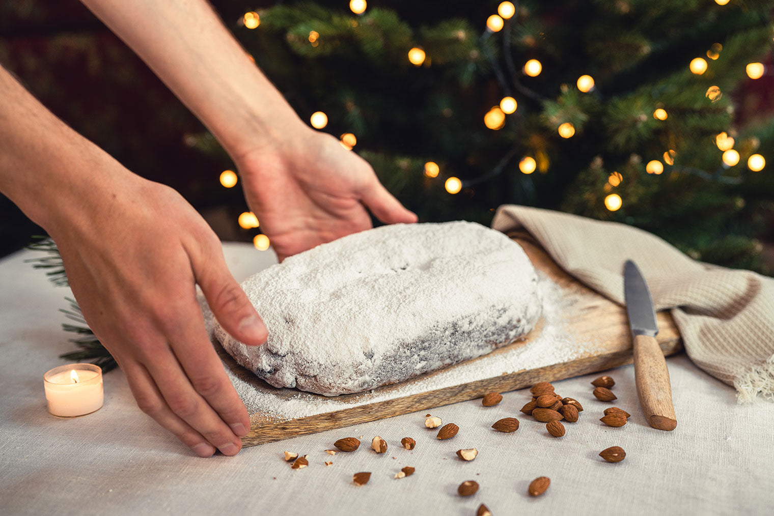 Gepuderter und unangeschnittener Mandelstollen wird von Handmodell präsentiert. Weihnachtlichkeit