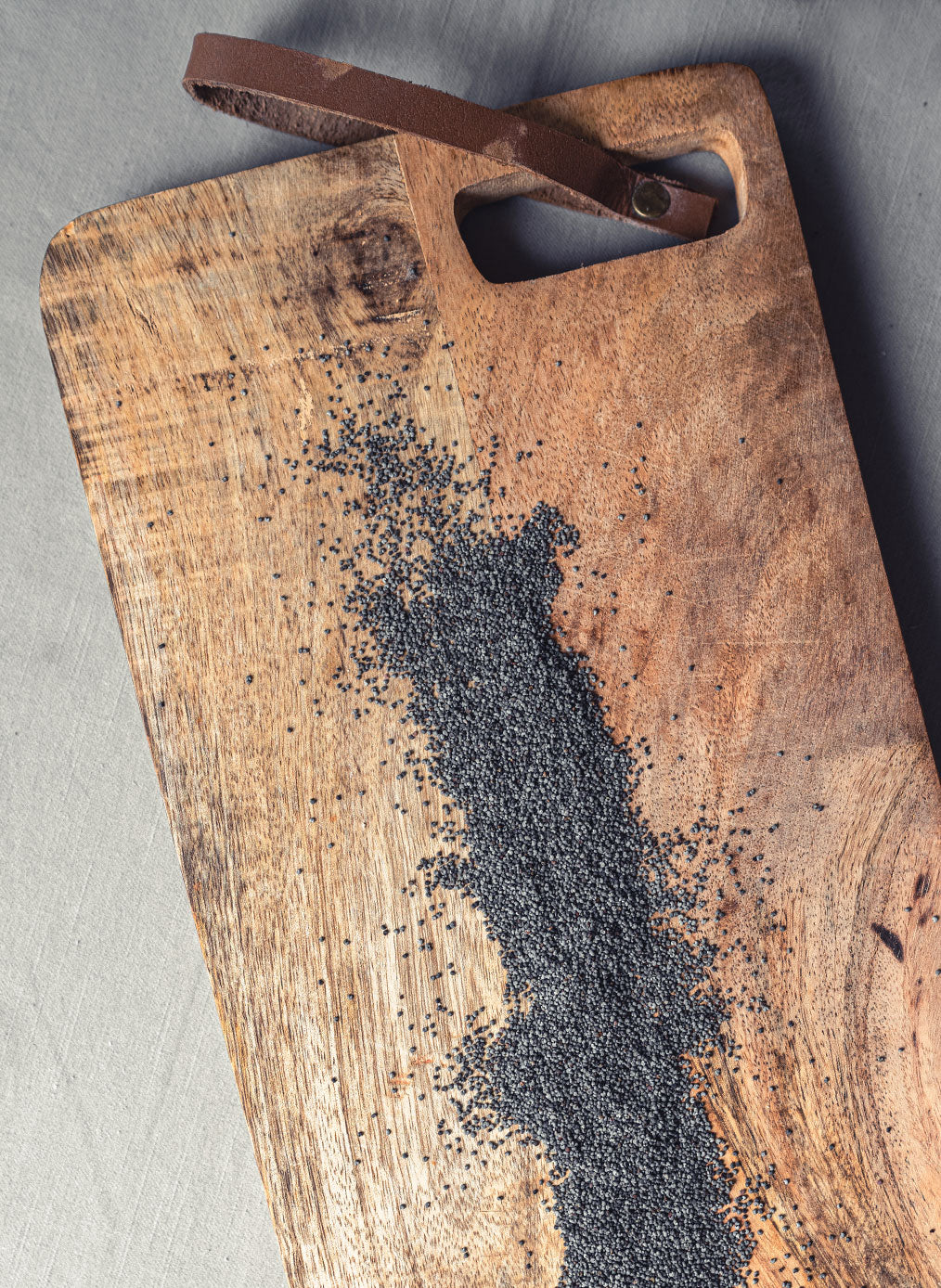 Hölzernes Schneidebrett mit Griff und ledernes Band, schwarze Mohnsamen auf der Oberfläche